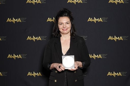 an image of Eliza Hull holding an award with AWMA logo wall