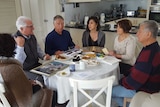 Six people sitting around a dining table looking at old photos