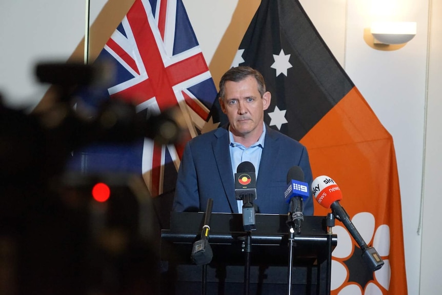 Michael Gunner stands in front of the Australian and NT flags at a press conference.