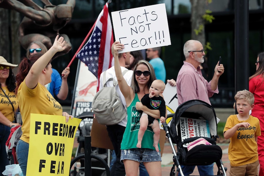 A woman carrying a baby holds up a sign saying 'facts not fear' in a protest.