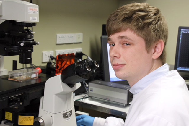 Student Aaron Beasley in a white lab coat in front of a microscope.