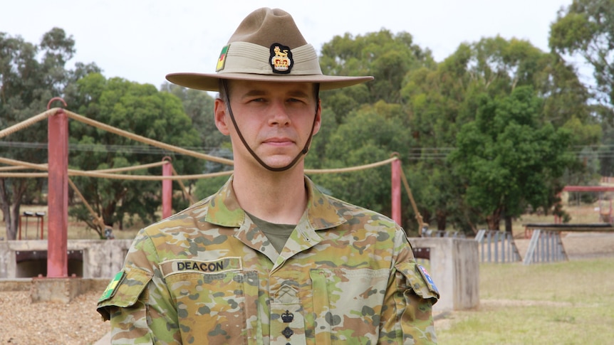 A man in army uniform and hat in front of an obstacle course