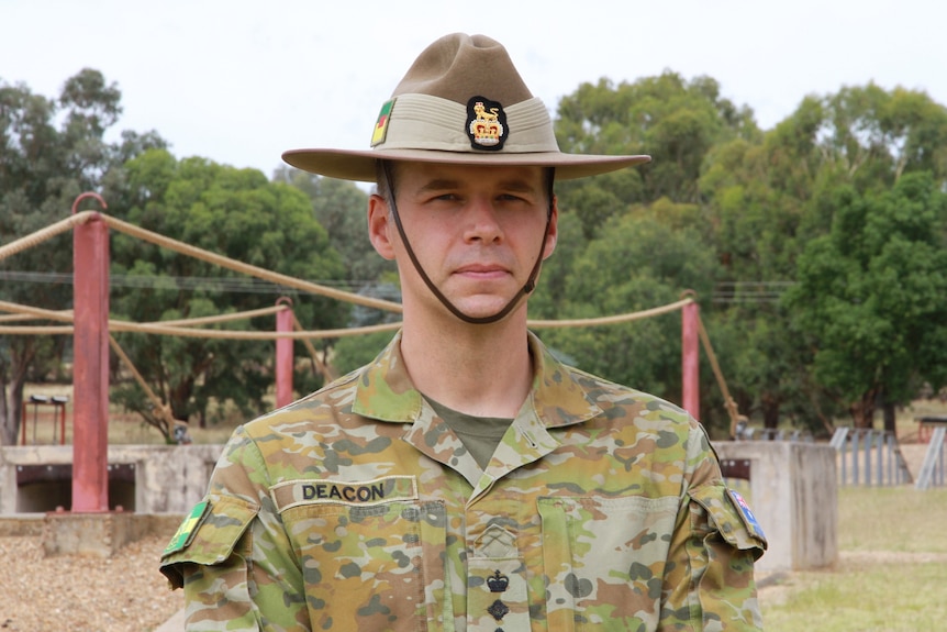 A man in army uniform and ghat infront of an obstacle course