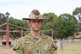 A man in army uniform and hat in front of an obstacle course
