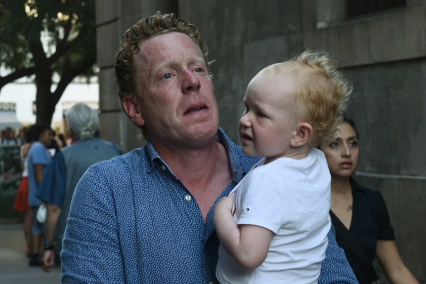 A man carrying a young child flees the scene of a car attack.