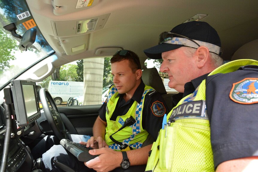 Police officers looking at newly fitted computer screen in police car.