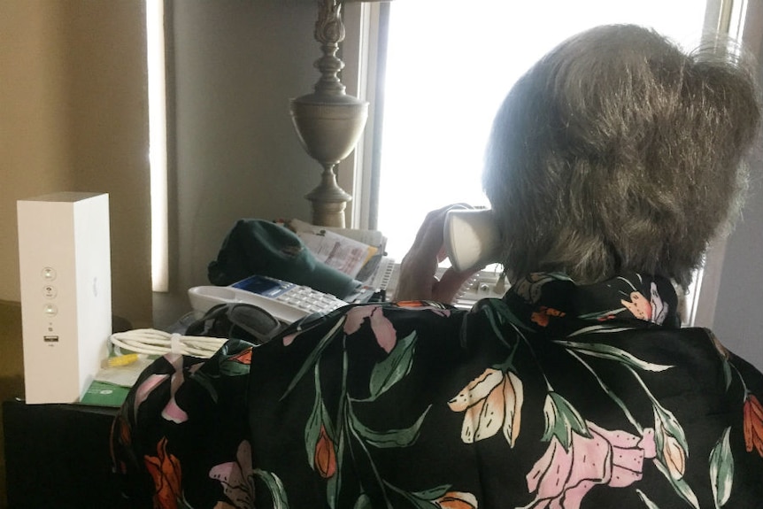 An elderly woman is seen from behind speaking on the phone.