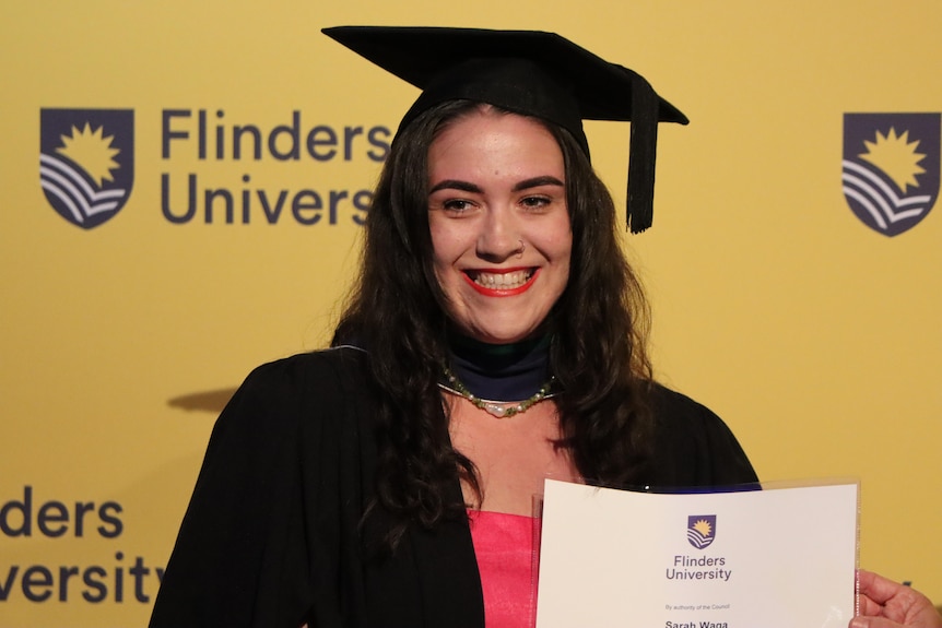Woman wearing university graduation hat hold certificate and smiles 