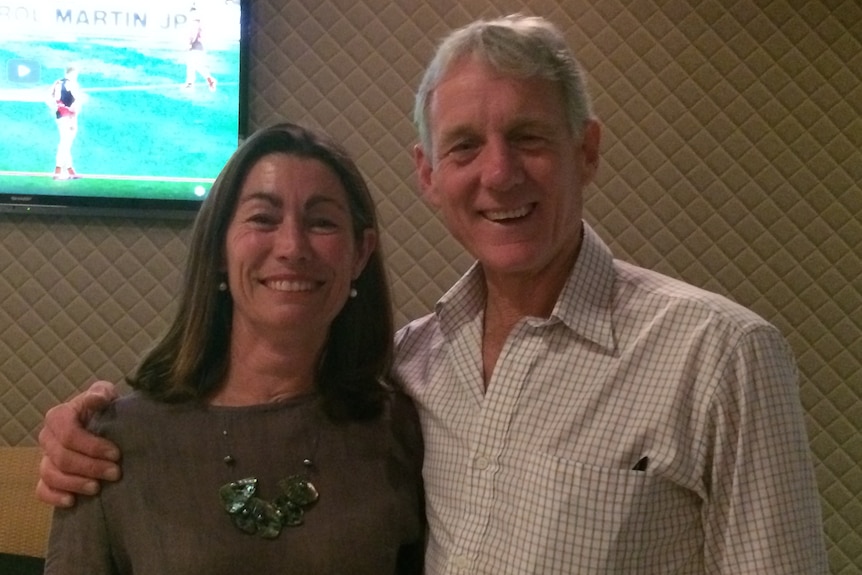 A man and a woman smiling at the camera with a projector screen behind them