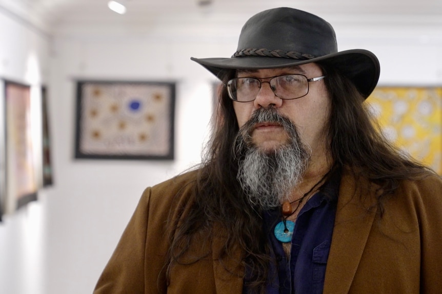 Aboriginal man with long hair and beard wearing a cowboy hat and blue pendant 