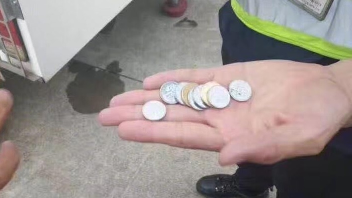 Staff member holds the nine coins, thrown by the elderly woman, in the palm of their hand.