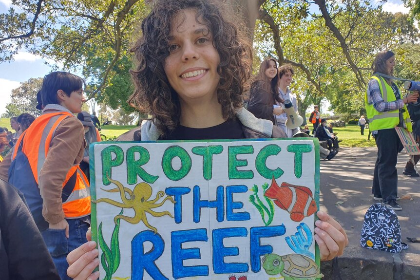 Arielle sostiene un cartel que dice proteger el arrecife.