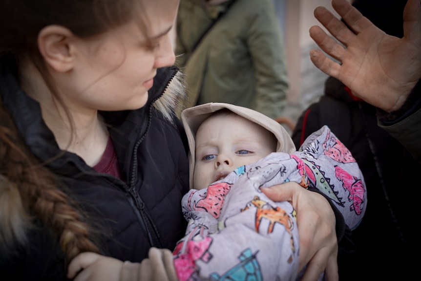 A young mum holds her son who has big blue eyes.