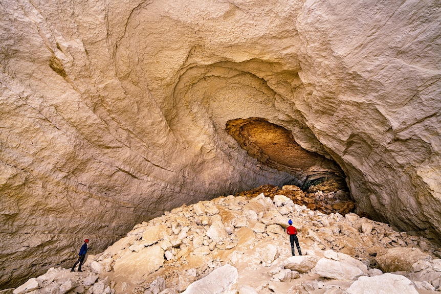 Two explorers standing on a rocky landscape that serves as the entrance to a cave.