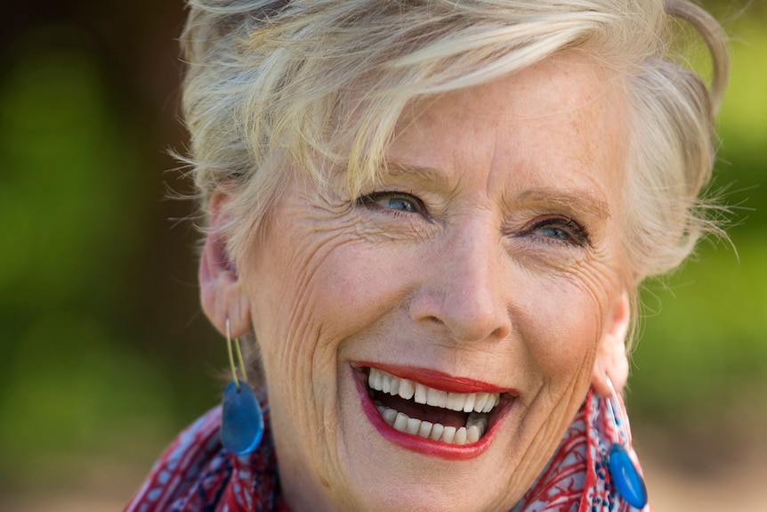 Maggie Beer has a big smile.  She has gray hair, cut short, and is wearing bright red lipstick and a scarf to match.