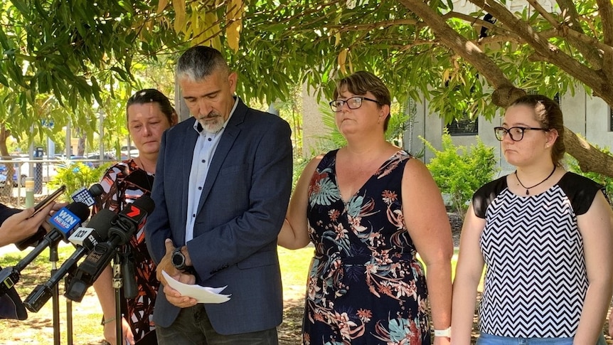 Mr Russo reads a statement, surrounded by family at a press conference under a tree.