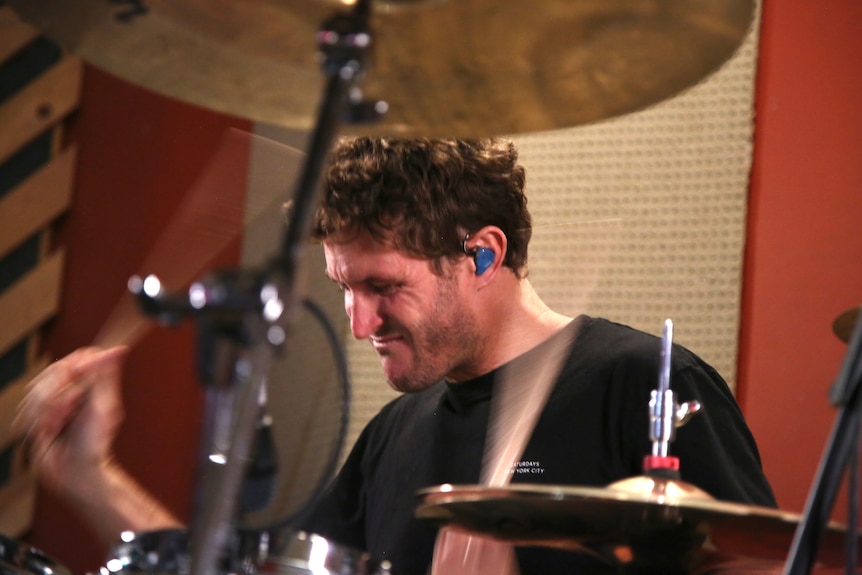 A man plays drums against a red and white stripe wall