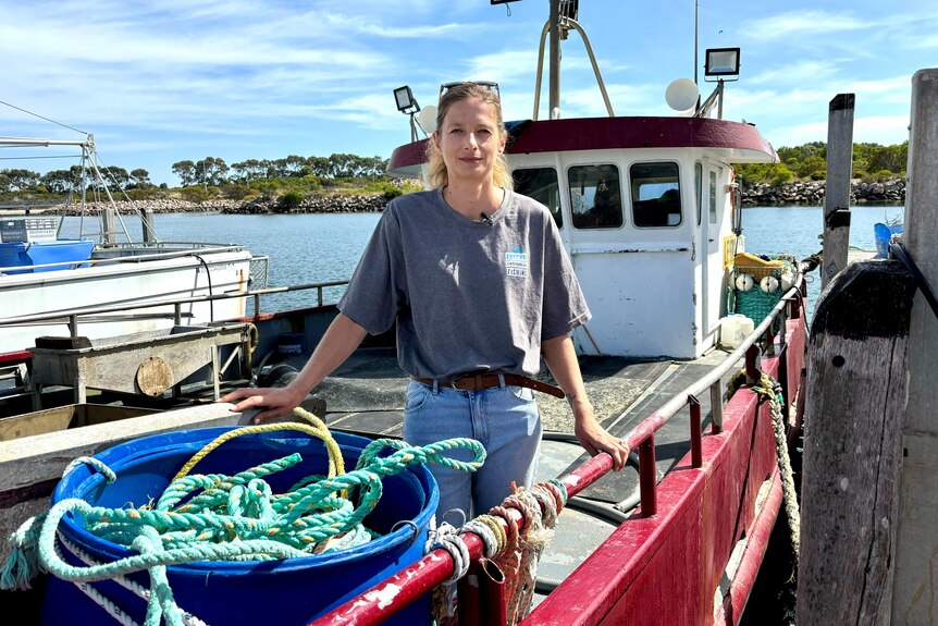 A woman in a t-shirt and jeans standing on a fishing boat. 