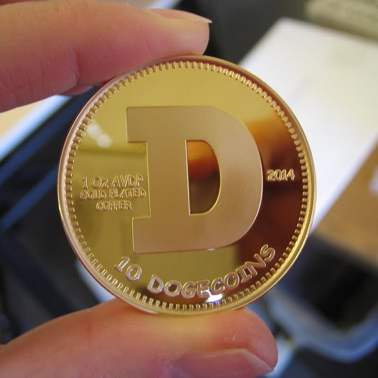 A photo of a gold 'Dogecoin' between two fingers
