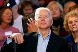 Joe Biden sits down on a chair at a campaign event in front of a crowd.