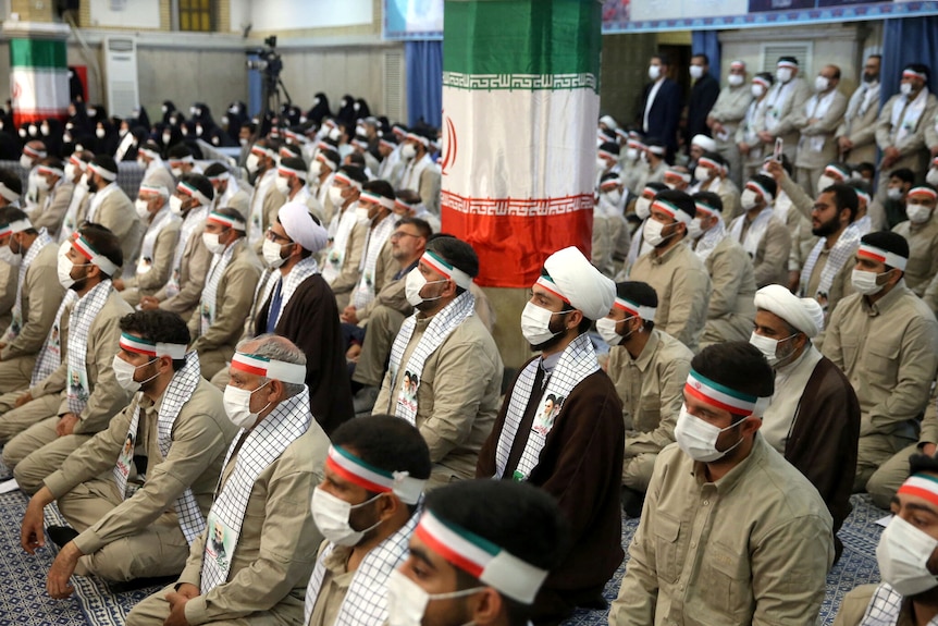 A group of people seated, dressed in khaki with Iran flag headbands
