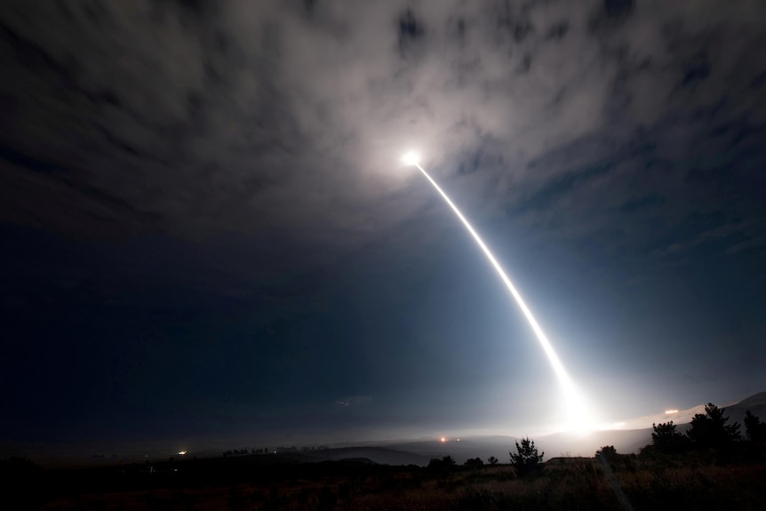 A bright white trail streams off a glowing projectile being launched high into the night sky.