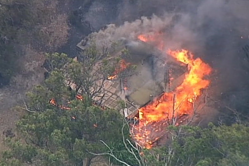 An aerial view of a home engulfed by smoke and flames.