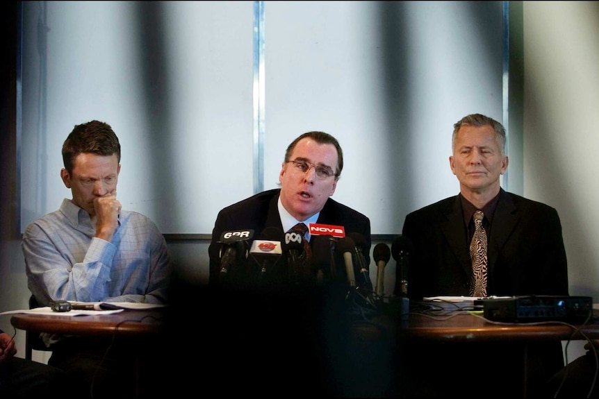 A lawyer speaks to the media, flanked by brothers with Ray and Peter Mickelberg.