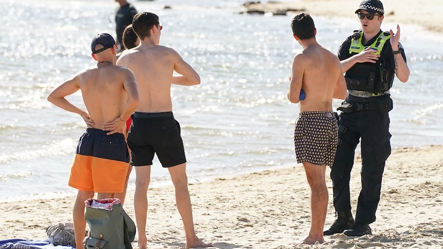 A police officer speaks to three men on a beach.