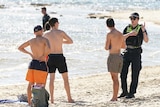 A police officer speaks to three men on a beach.