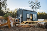 A grey-coloured tiny cabin with a bathtub on the deck on a farm.