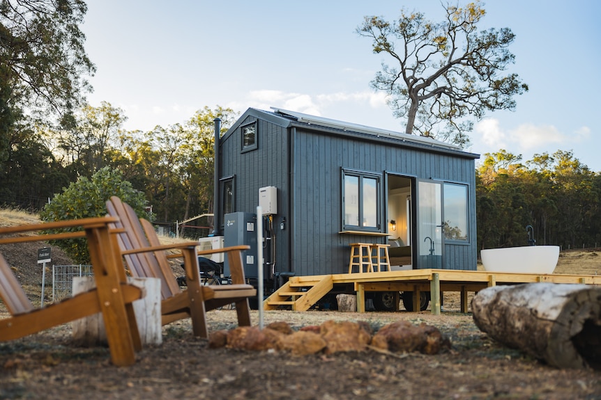 A grey-coloured tiny cabin with a bathtub on the deck on a farm.