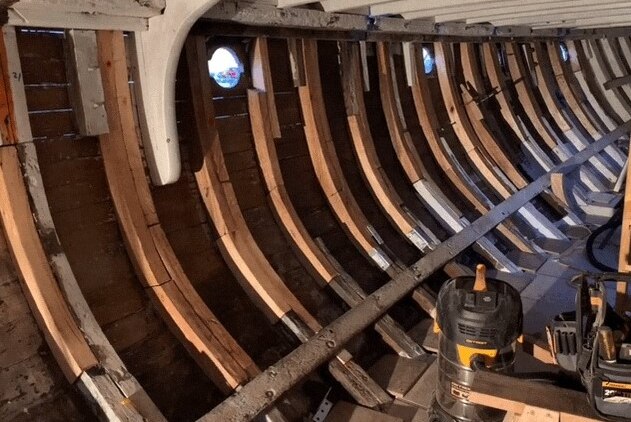 Photograph of the stripped back inside of an old yacht showing curved beams going down into the hull