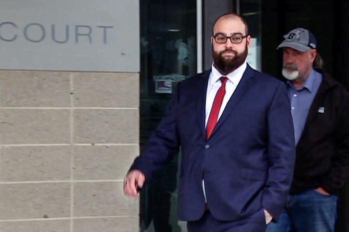 A man in a suit walks out of a court building.