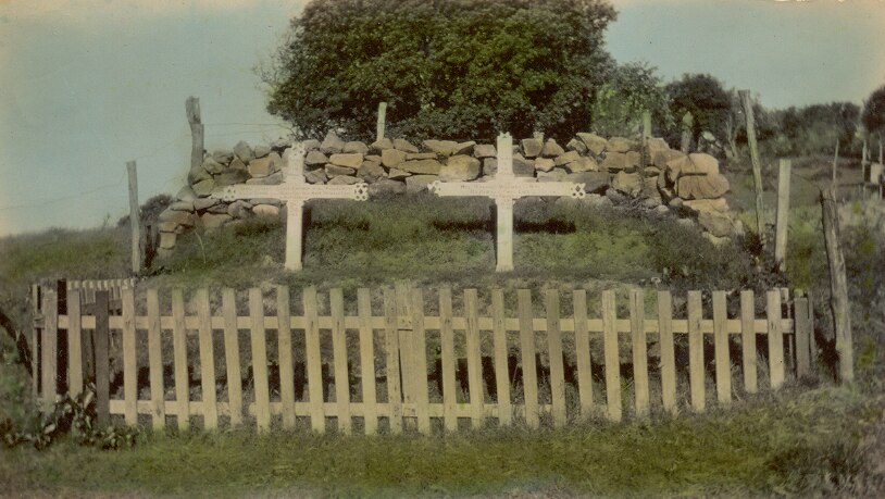 Two white wooden crosses over a mound burial site, surrounded by a small wooden fence.