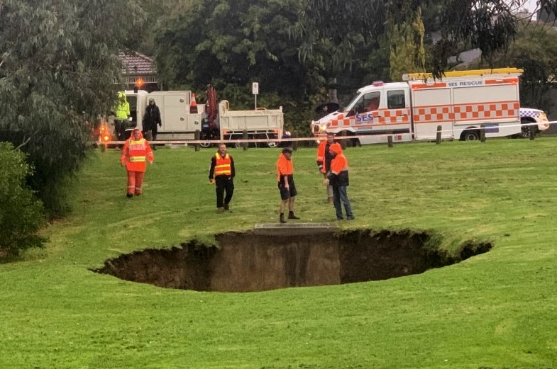 SES officers stand beside a large sinkhole.
