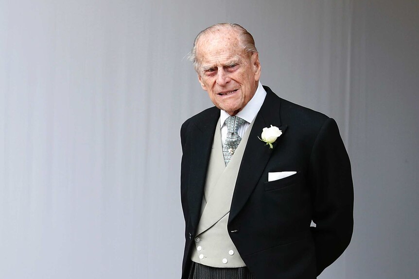 Elderly Prince Philip wearing black tuxedo, grey vest and white flower on lapel