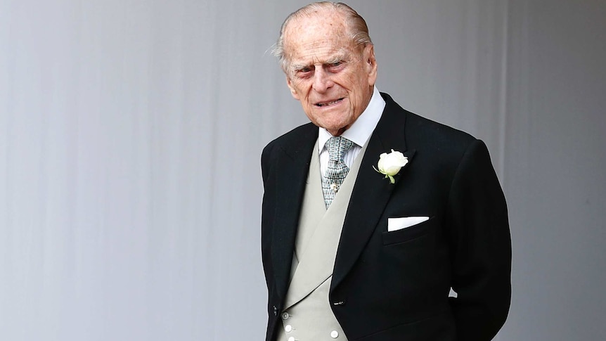 Elderly Prince Philip wearing black tuxedo, grey vest and white flower on lapel