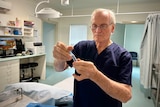 A man in medical scrubs fills a syringe in a medical surgery room