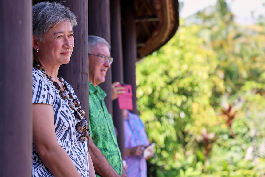 Penny Wong stands in casual clothes in an entrance to a building watching a welcome at a resort in Samoa. 