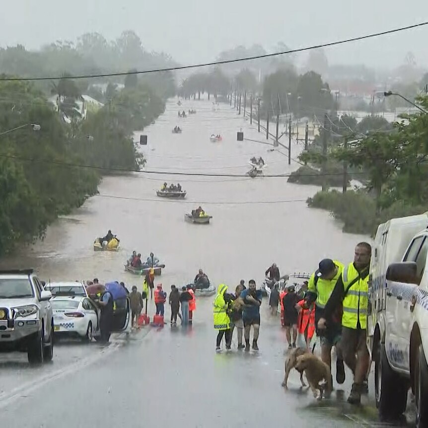 A flooded street with boats and rescue vehicles and people