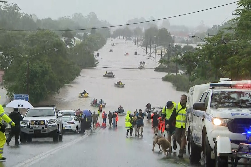 A flooded street with boats and rescue vehicles and people.
