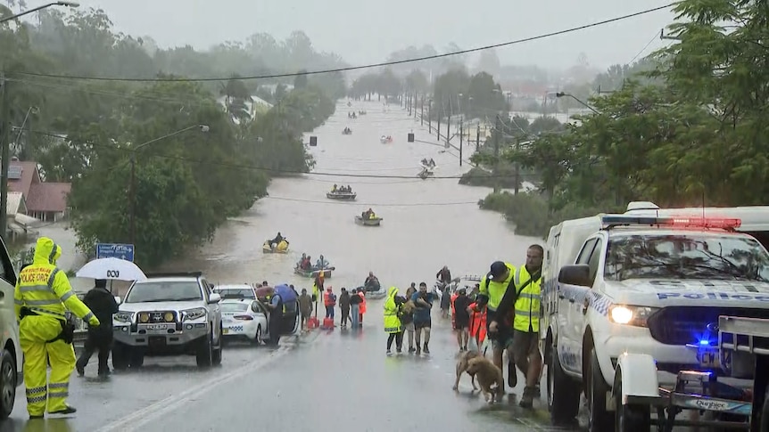 A flooded street with boats and rescue vehicles and people