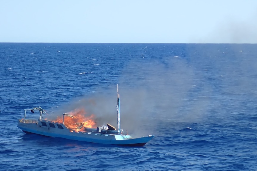 A burning boat in the middle of the ocean