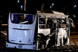 A destroyed tourist bus sits on a the side of a road with its side windows and doors blown off by a bomb.