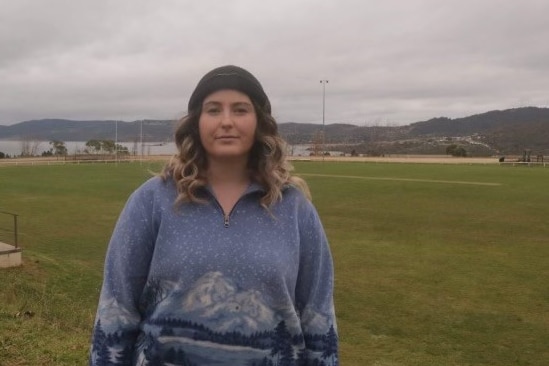 A woman in a jumper and beanie on an oval.
