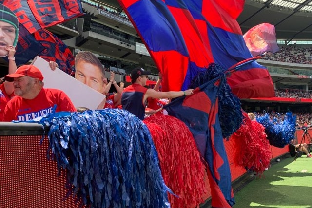 Melbourne AFL fans sit in the stands at the MCG waving flags and floggers during a premiership celebration.