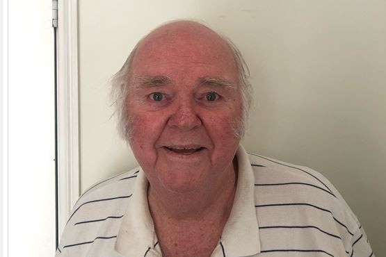 Man with a white collared shirt stares with smiling eyes at camera. 