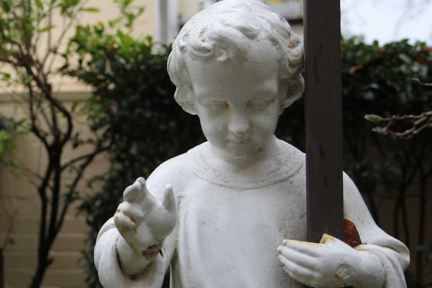 A statue stands holding a wooden cross in the Sisters of Charity convent garden in Darlinghurst.