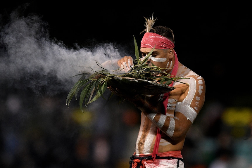 An Indigenous performer conducts a traditional smoking ceremony at the NRL match